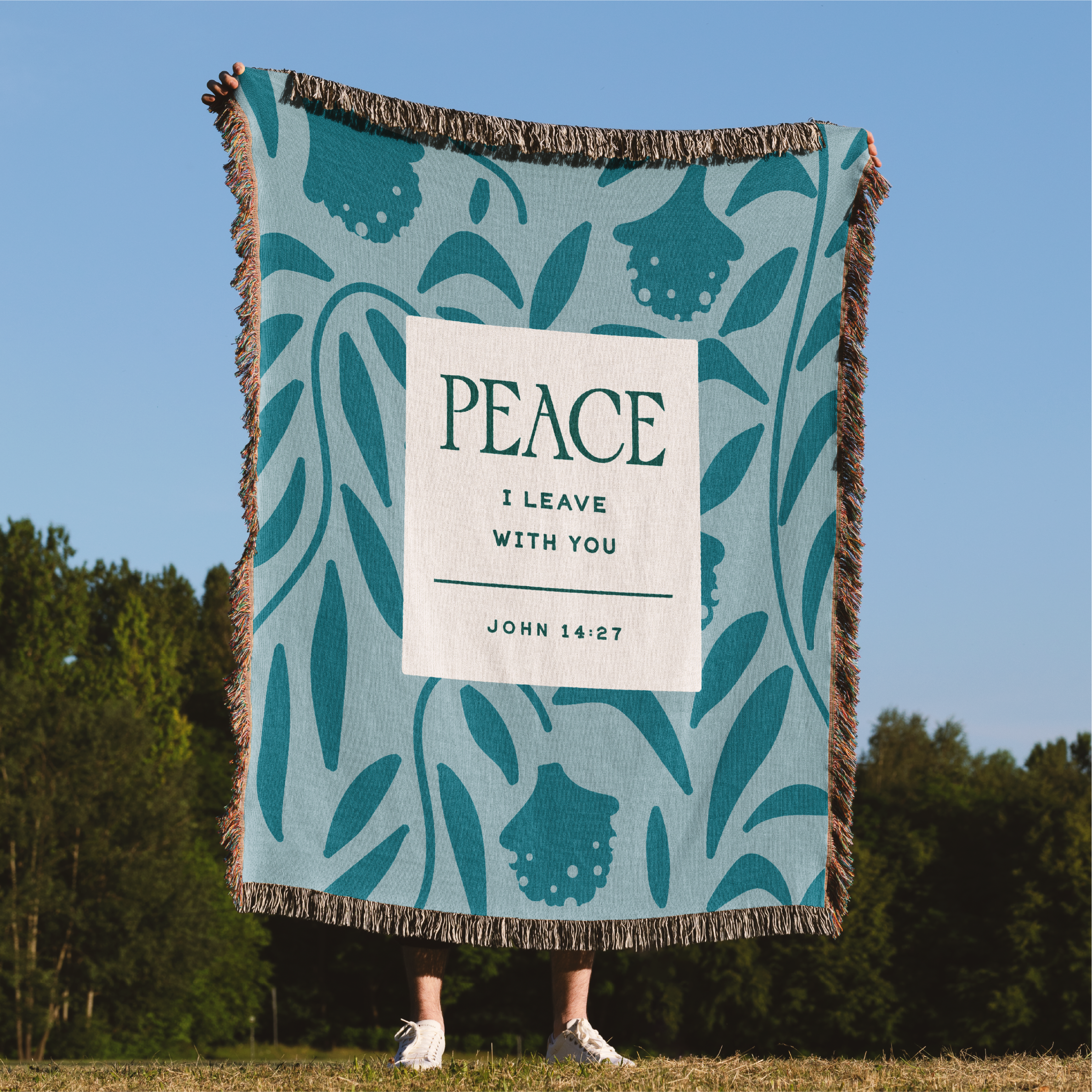 Blanket with 'Peace' text and nature design, held by a person outdoors.