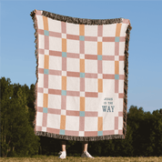 Checkered blanket with 'Jesus is the Way' text on a grassy field with trees in the background
