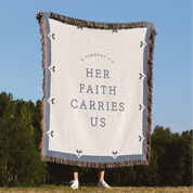 Blanket with 'Her Faith Carries Us' text in a natural setting