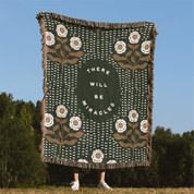 Decorative blanket with floral patterns and 'There will be miracles' text, displayed outdoors.