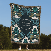 Decorative blanket with floral design and text against a blue sky and green trees background