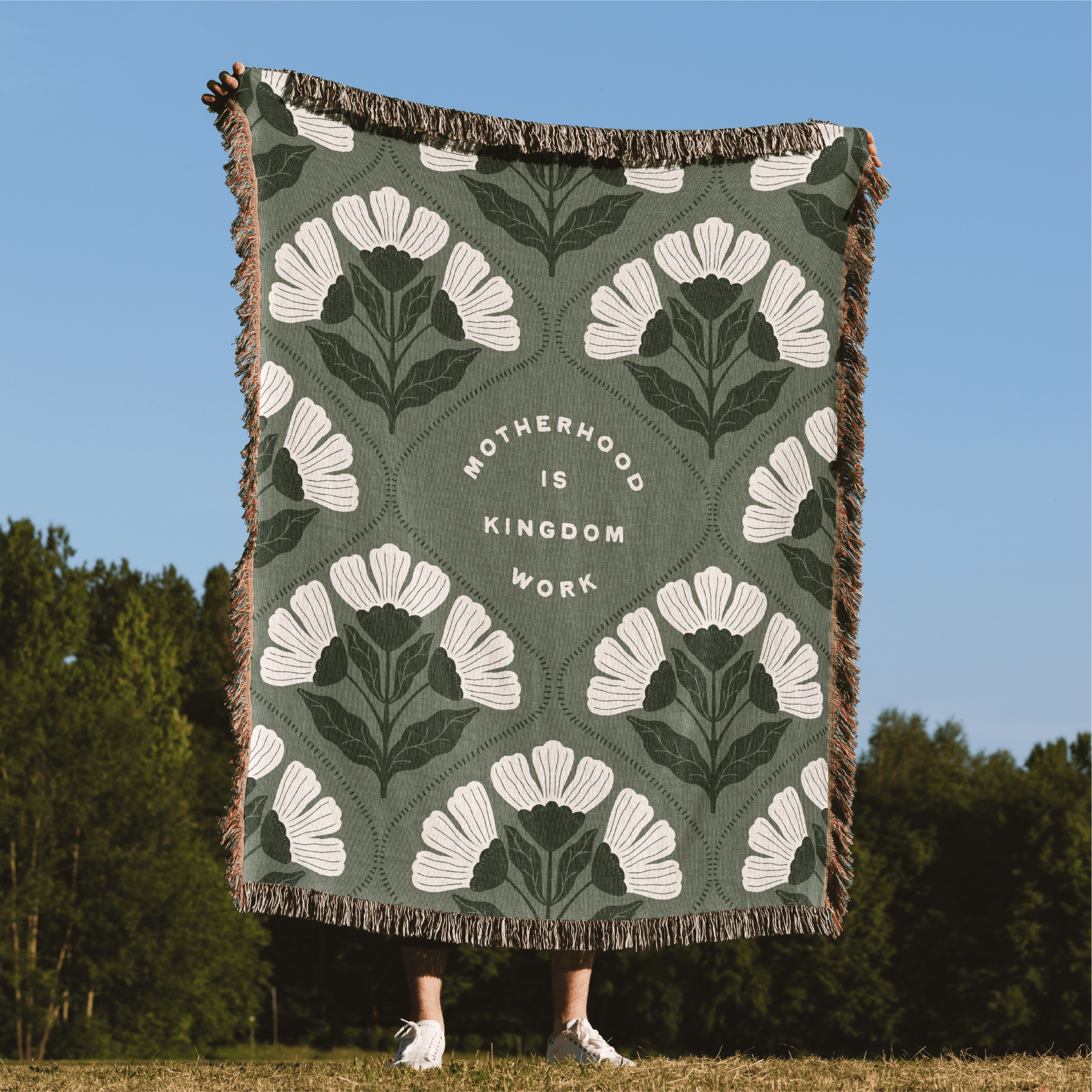 Floral patterned throw blanket with text on a grassy field with trees in the background