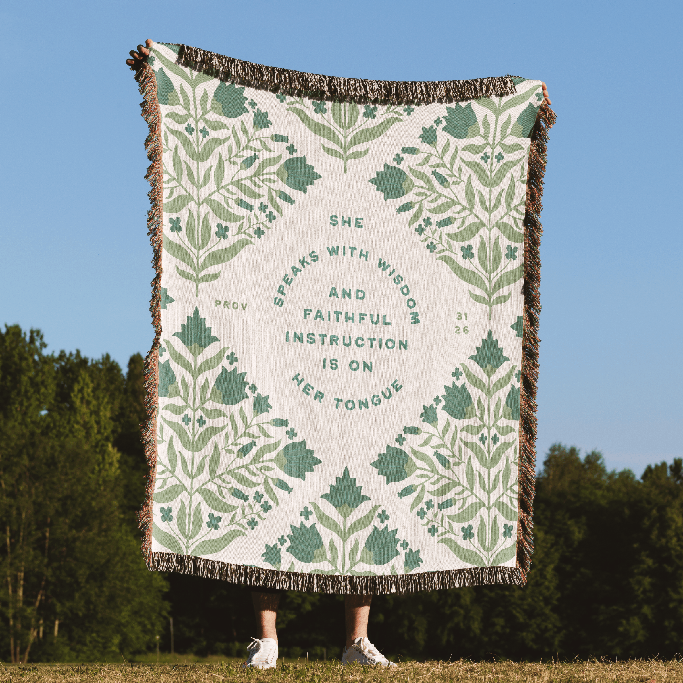 Decorative throw blanket with green floral pattern and text, displayed outdoors.