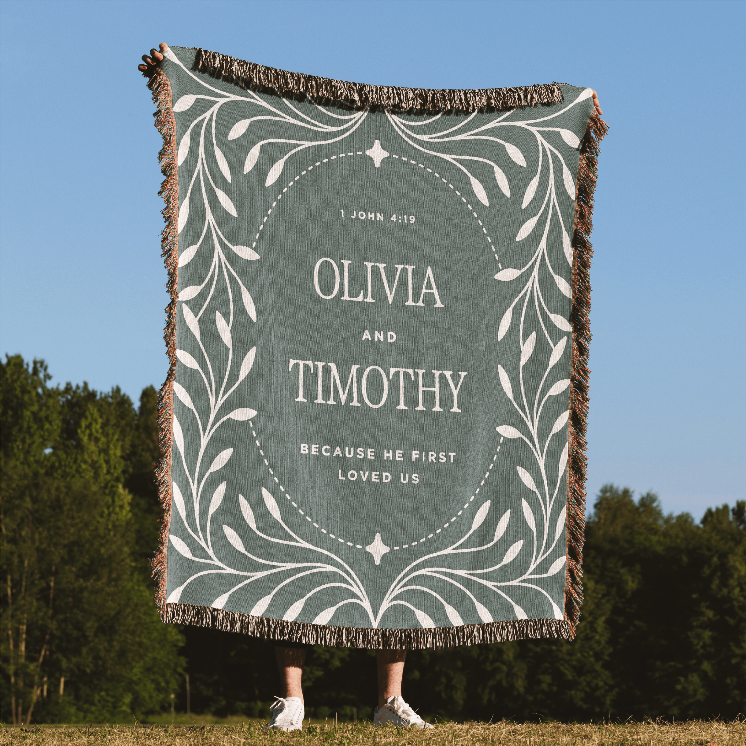 Blanket with 'Olivia and Timothy' text in a decorative frame, held by a person outdoors.