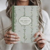 Person holding a book titled 'Pray About It' with floral design
