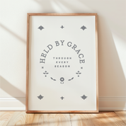 Framed print with 'Held by Grace, Through Every Season' text on a white background