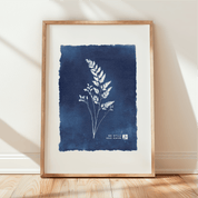 Framed artwork with blue background and white plant illustration on a light wooden floor.