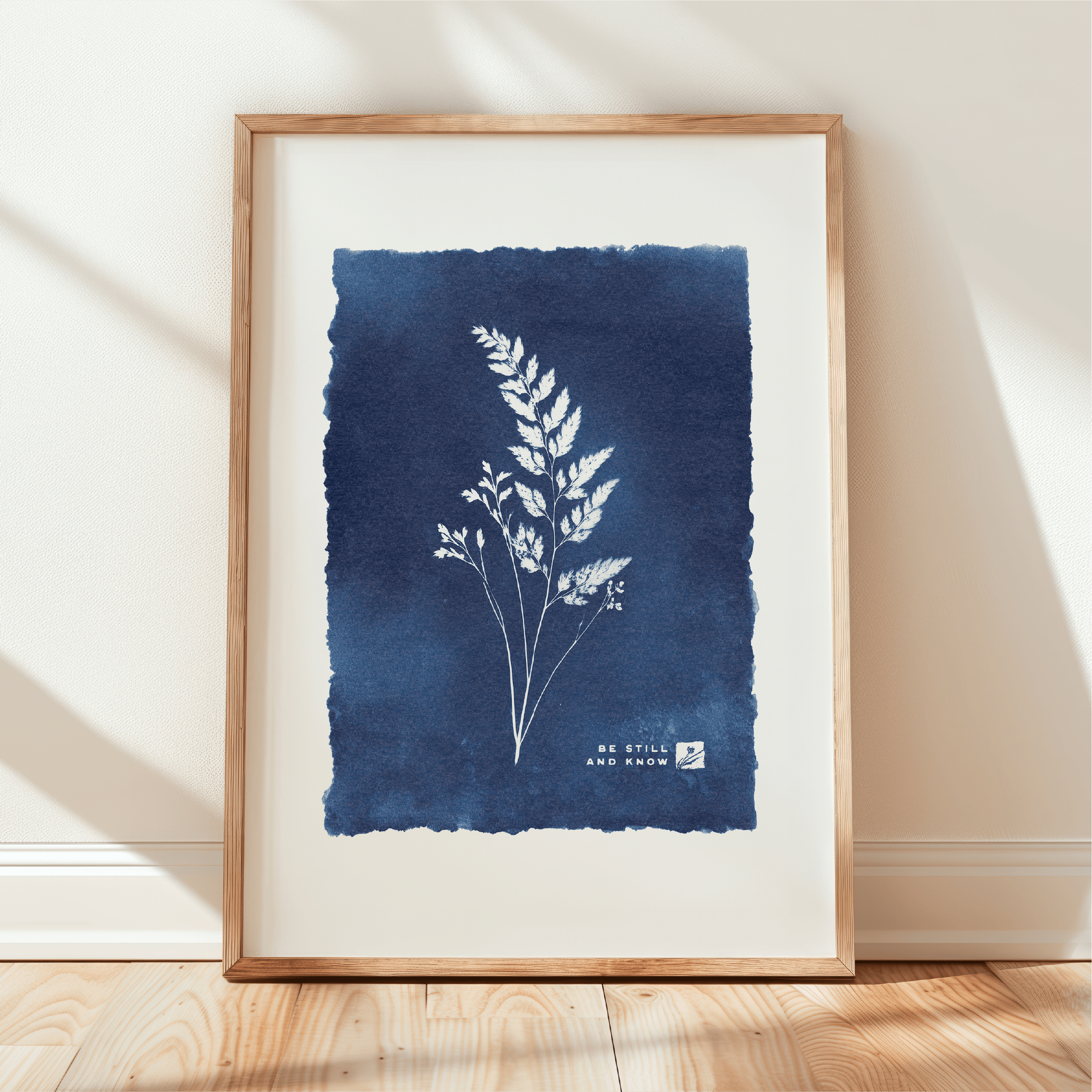 Framed artwork with blue background and white plant illustration on a light wooden floor.
