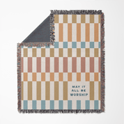 Checkered blanket with text 'May it all be worship' on a white background