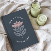 Gray notebook with floral design and text on a light fabric background with two green candles.