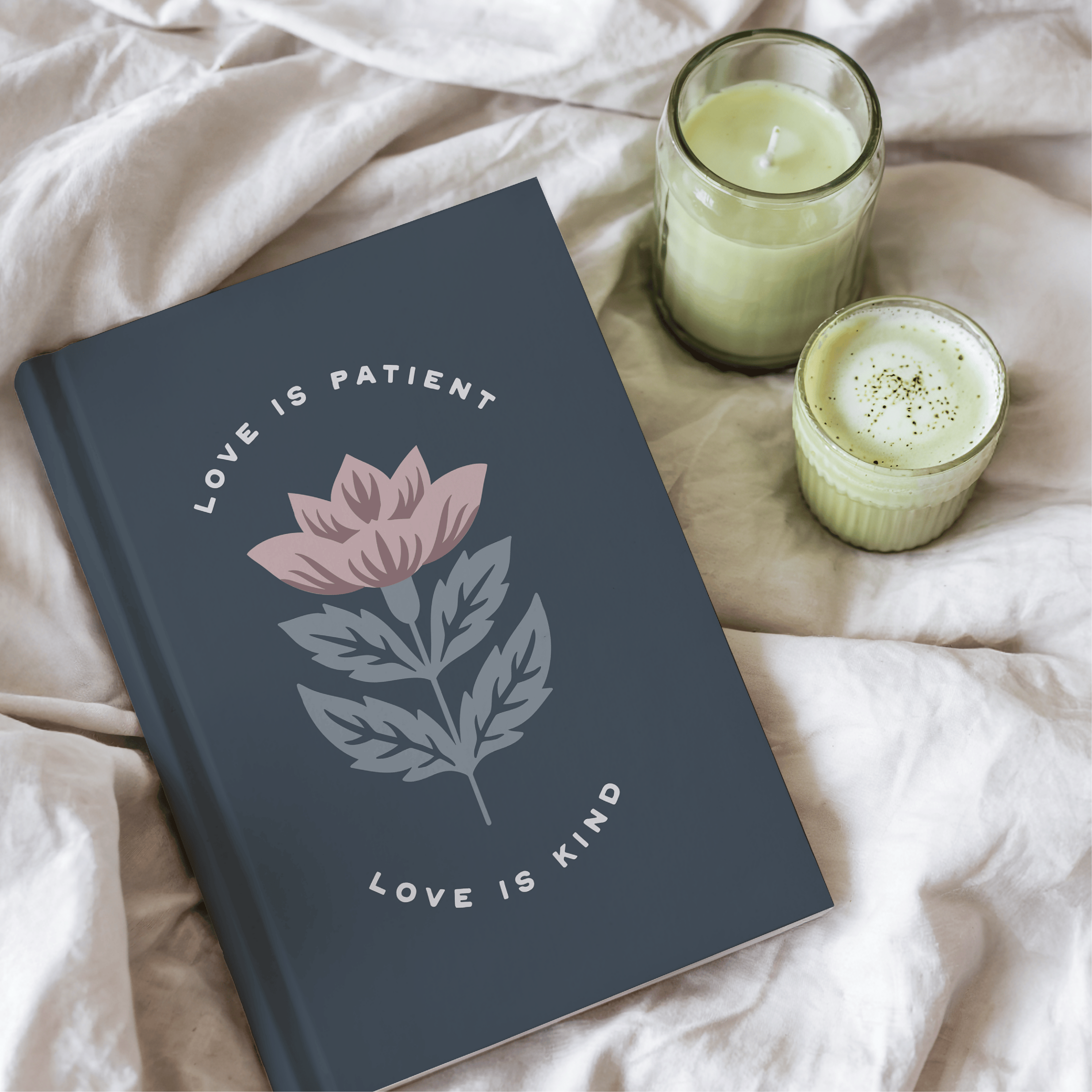 Gray notebook with floral design and text on a light fabric background with two green candles.
