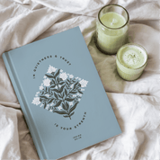 Blue notebook with floral design and text on a light pink surface with two candles.