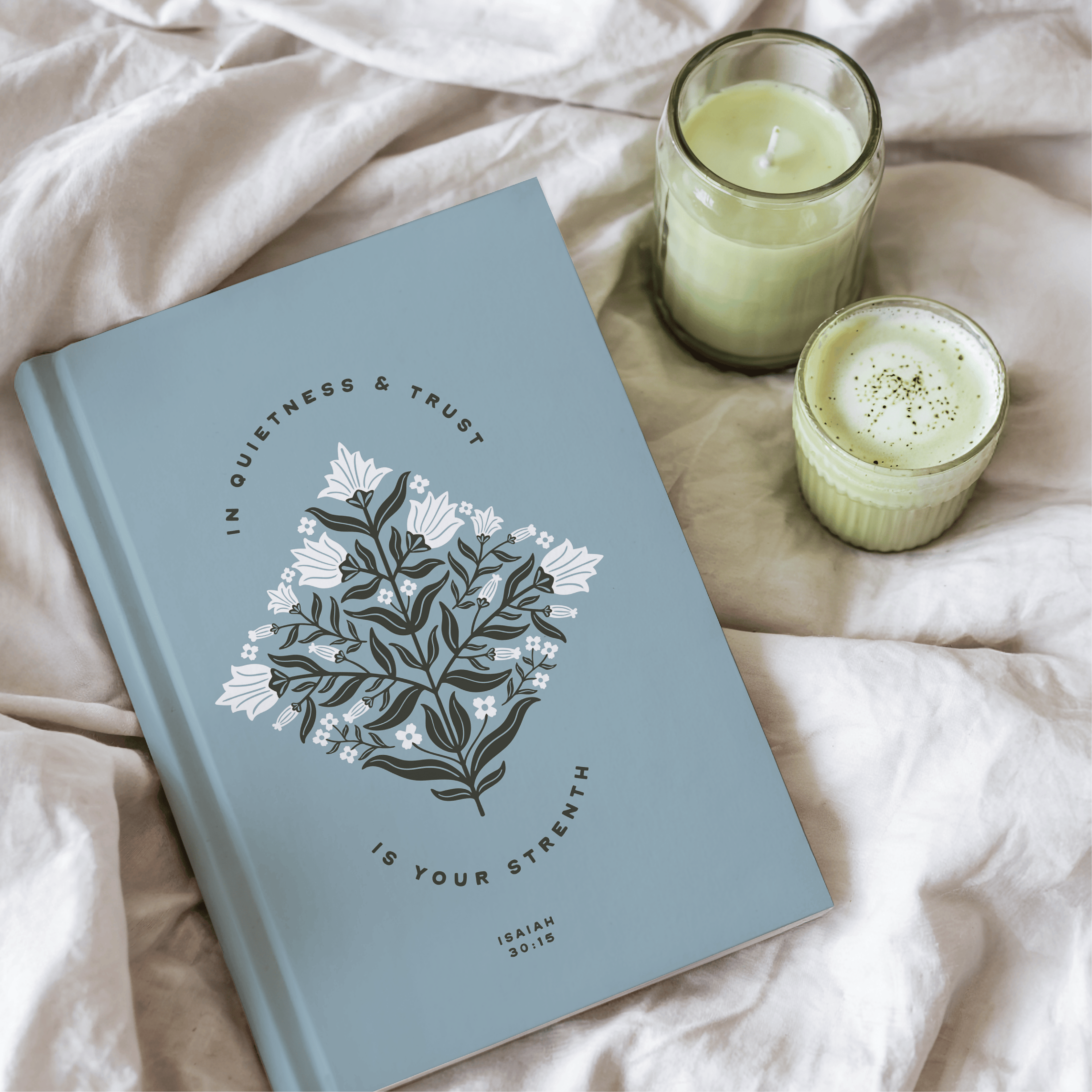 Blue notebook with floral design and text on a light pink surface with two candles.