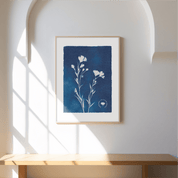 Framed artwork with a blue square and white floral design on a white wall.