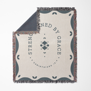 Blanket with 'Strength is found by grace' text and decorative border on a white background