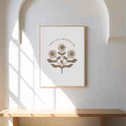 Framed artwork with floral design and text on a wall with sunlight casting shadows.