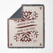 Blanket with floral design and text 'Abide in me, and I in you' from John 15:4 on a white background