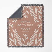 Blanket with leaf pattern and text 'Peace be to this house Luke 10:18' on a white background