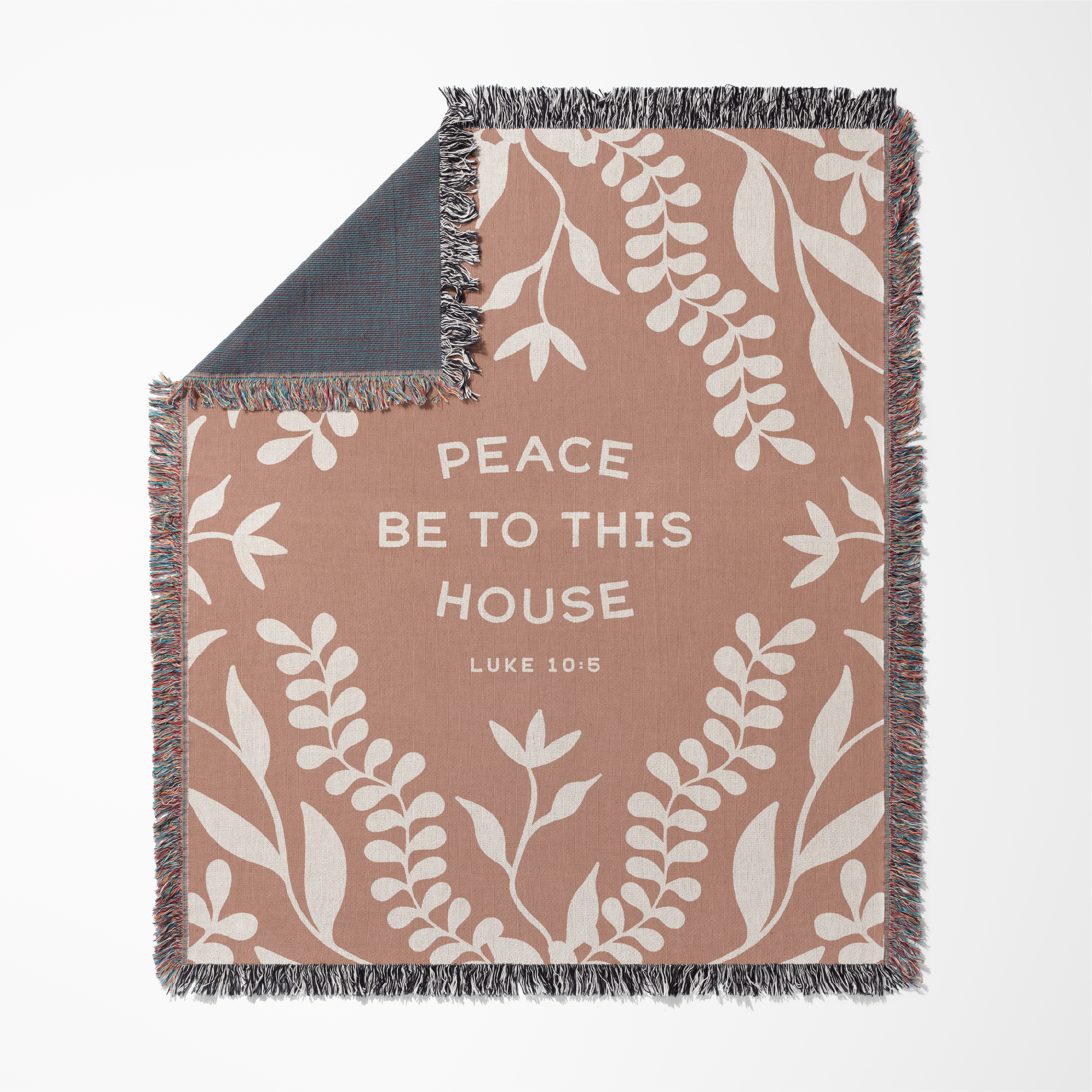 Blanket with leaf pattern and text 'Peace be to this house Luke 10:18' on a white background
