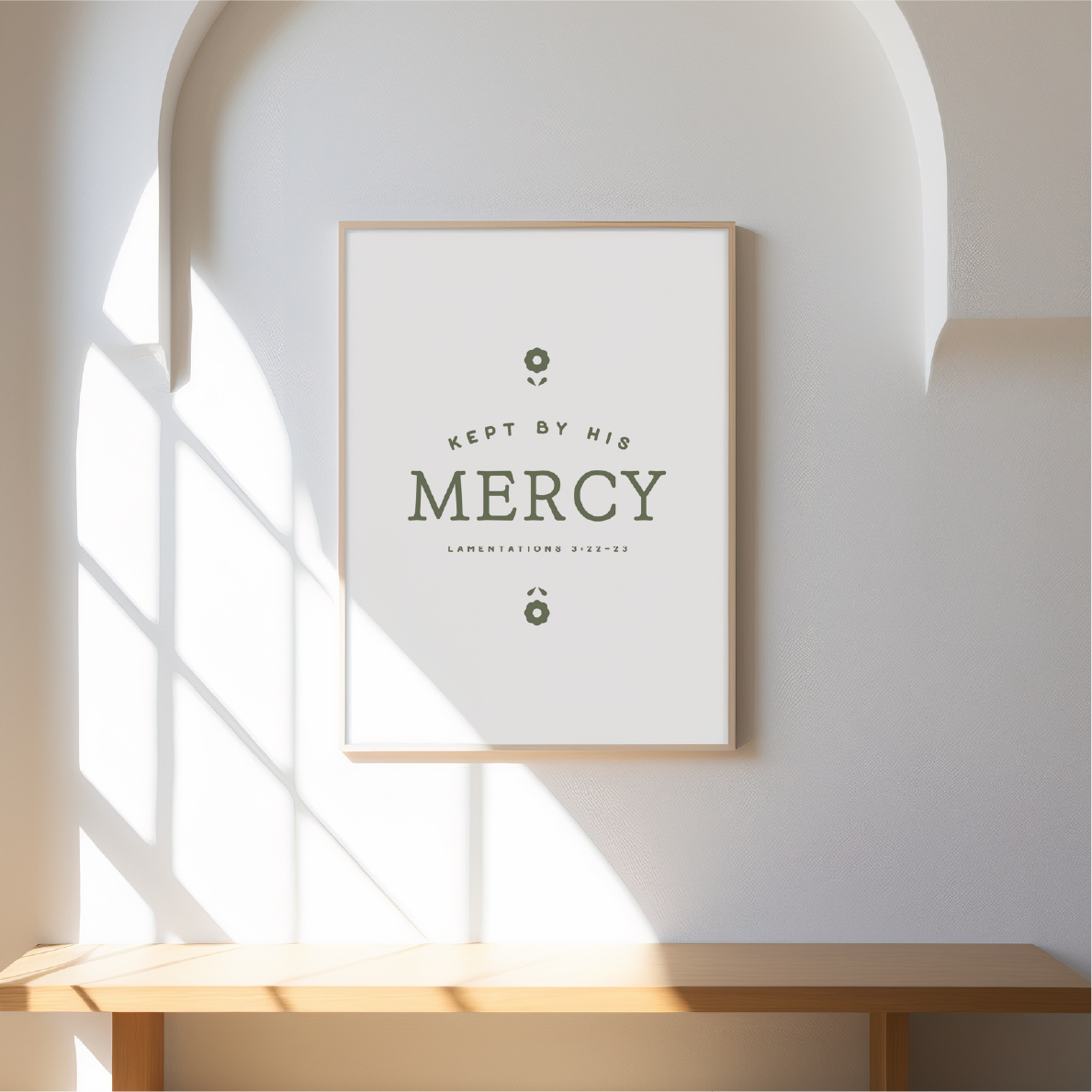 Framed artwork with 'Keep me by His Mercy' text on a wall with sunlight filtering through.