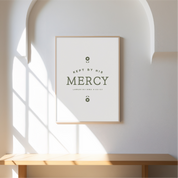 Framed artwork with 'Keep me by His Mercy' text on a wall with sunlight filtering through.