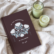 Mauve notebook with floral design and text on a light fabric background with two candles.