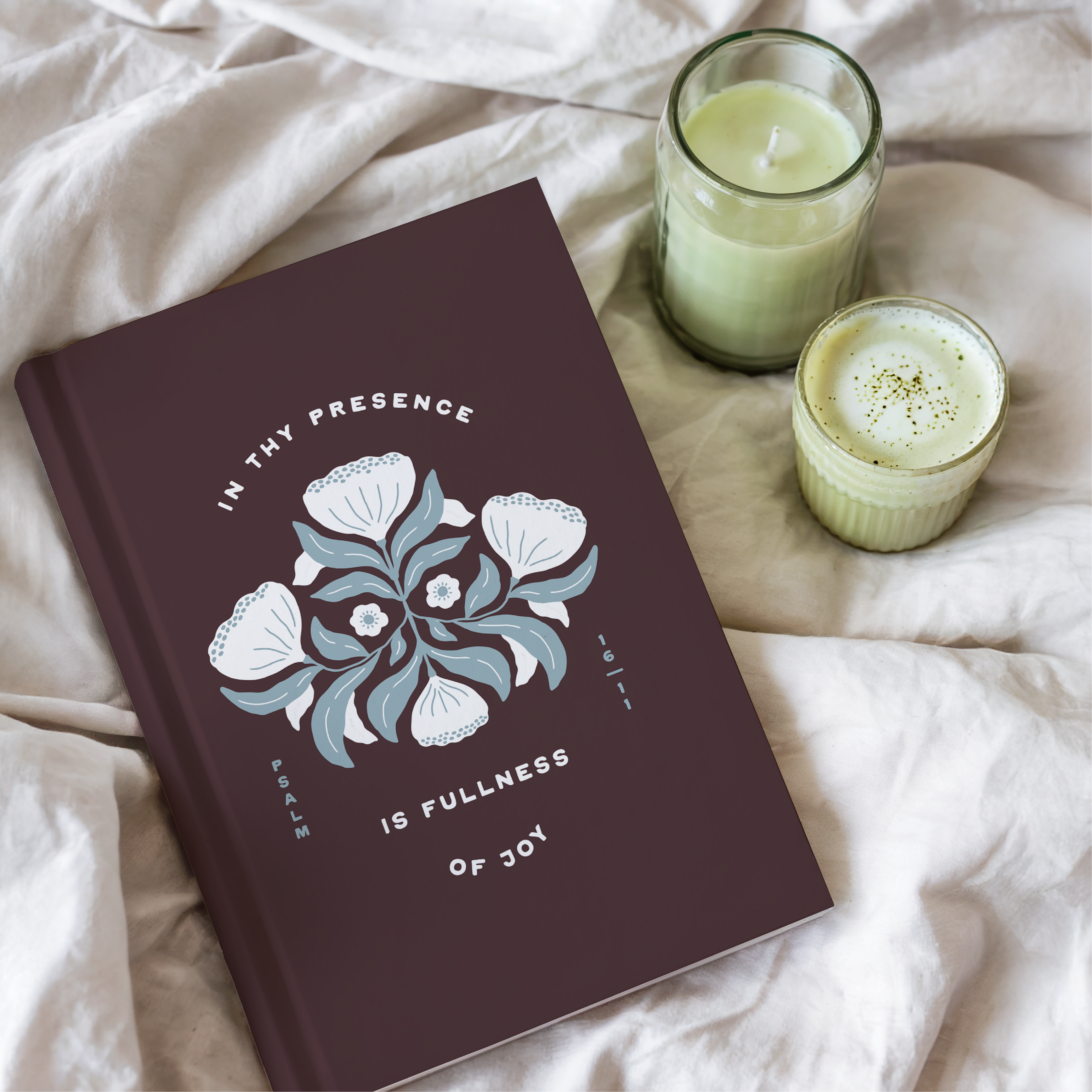Mauve notebook with floral design and text on a light fabric background with two candles.