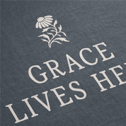 Text 'GRACE LIVES HERE' with a floral design on a dark fabric background
