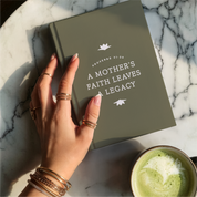 Hand holding a green book with text on a marble surface next to a cup of green tea.