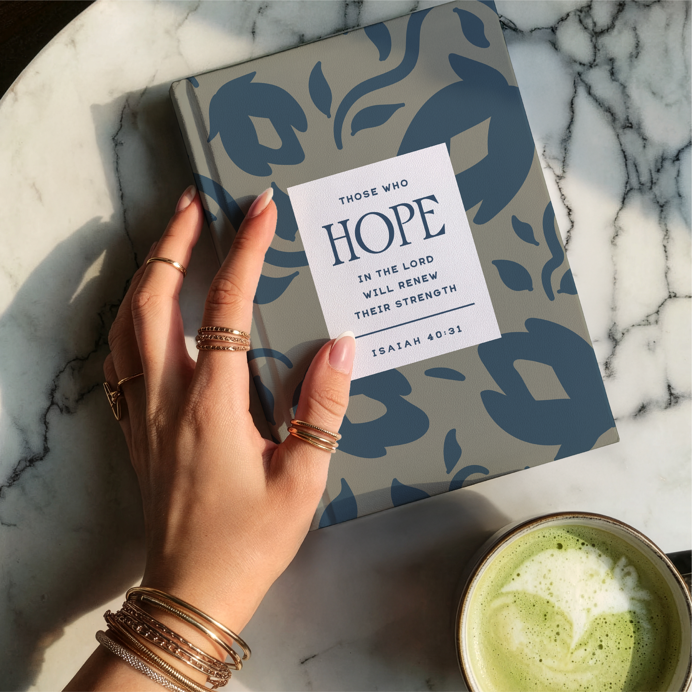 Hand holding a card with a motivational quote over a notebook on a marble surface with a cup of green tea.
