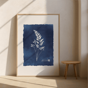 Framed artwork with blue background and white plant design on a beige wall.