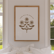 Framed artwork with floral design and text on a wall in a room with windows.