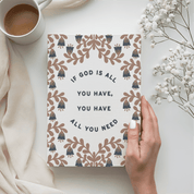 Notebook with motivational quote held by a hand, next to a cup of coffee and flowers on a light surface.