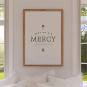 Framed artwork with 'Kept by His Mercy' text on a wall in a room with windows.