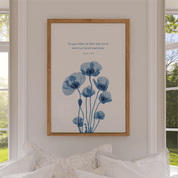 Framed artwork with blue floral design and text on a wall above a bed.