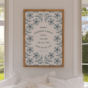 Framed artwork with floral design and text on a wall in a room with windows.
