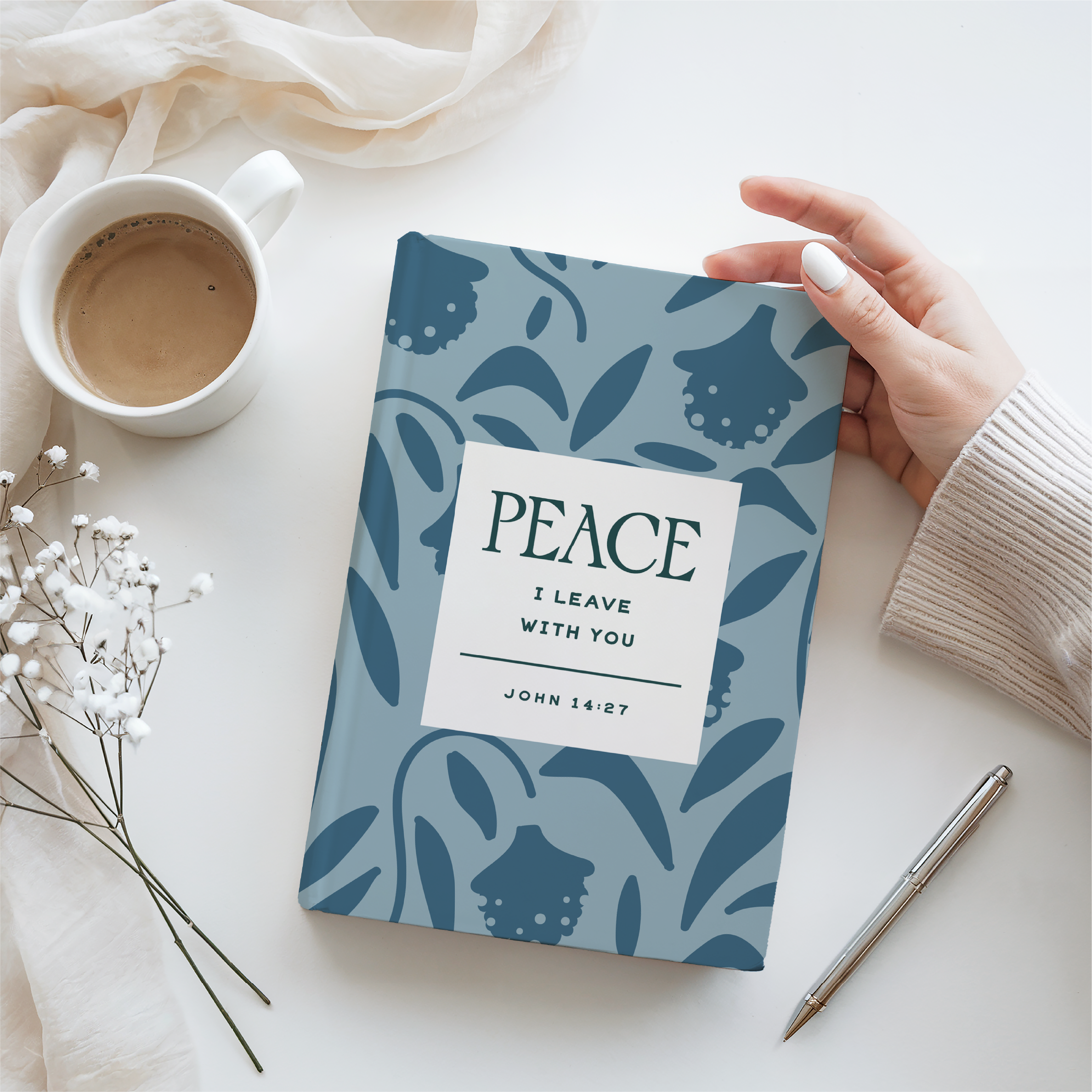 Notebook with 'Peace' quote held by a hand on a white surface with a cup and pen.