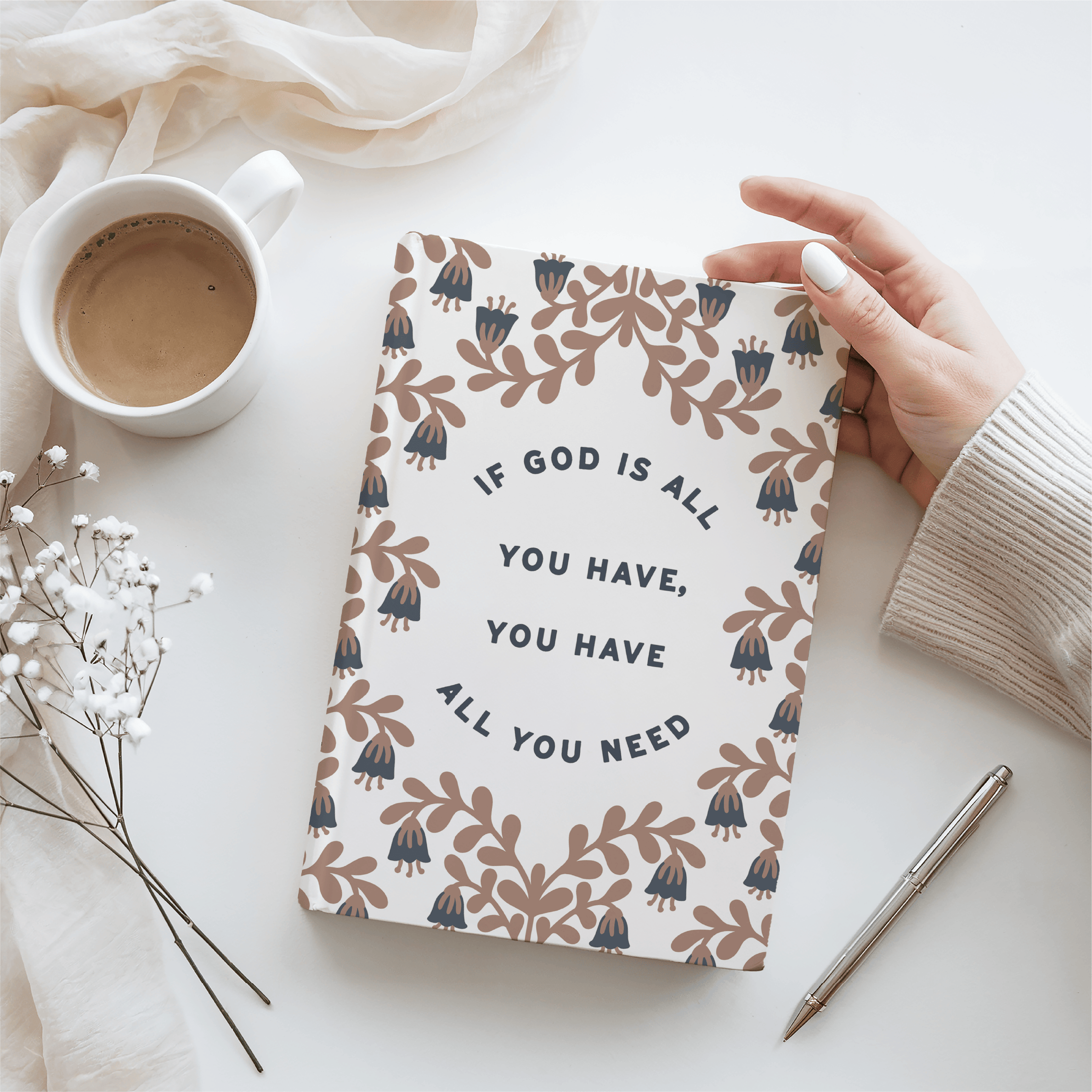 Notebook with motivational quote held by a hand on a white surface with a cup and pen.