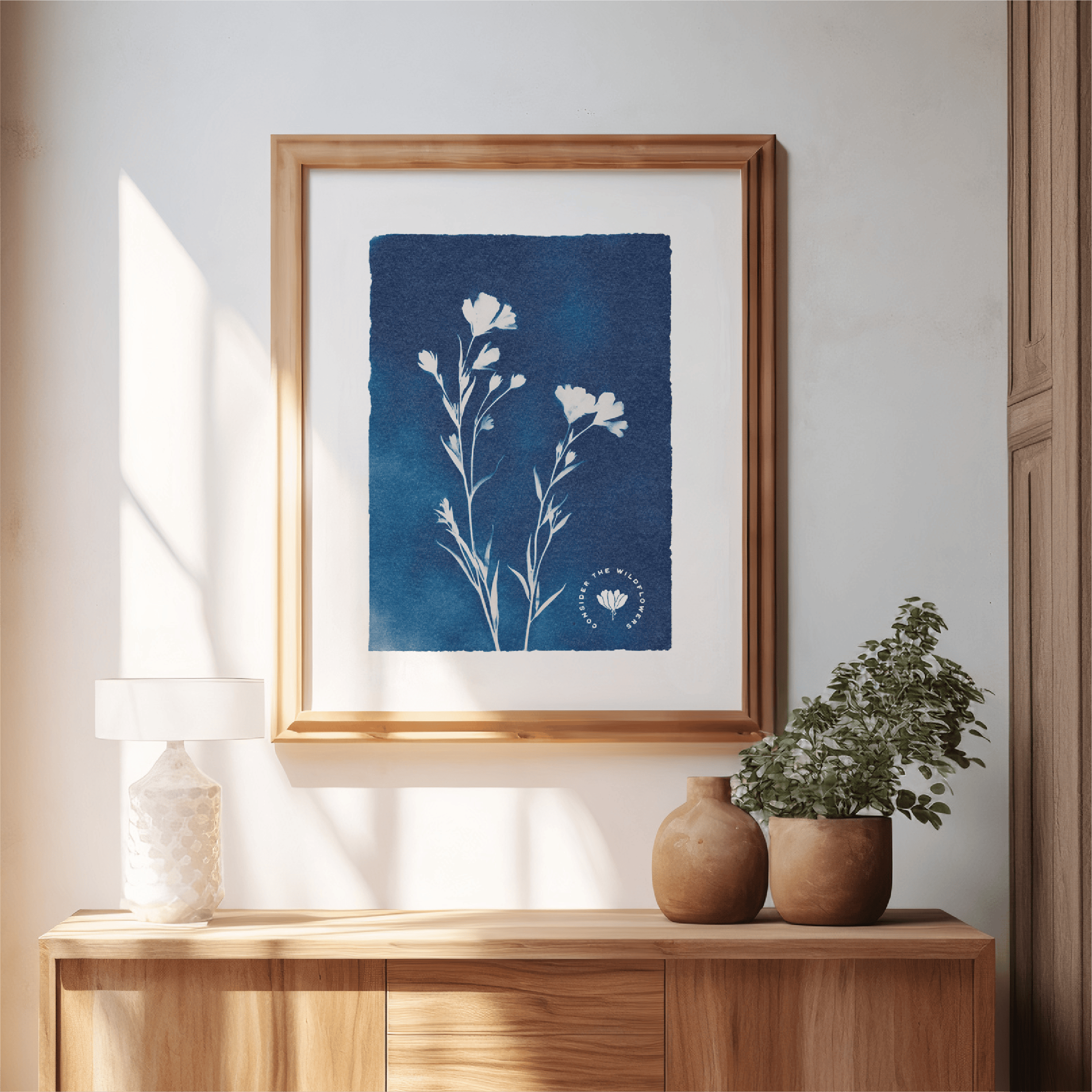 Framed botanical print on a wall above a wooden console table with decorative vases and plants.