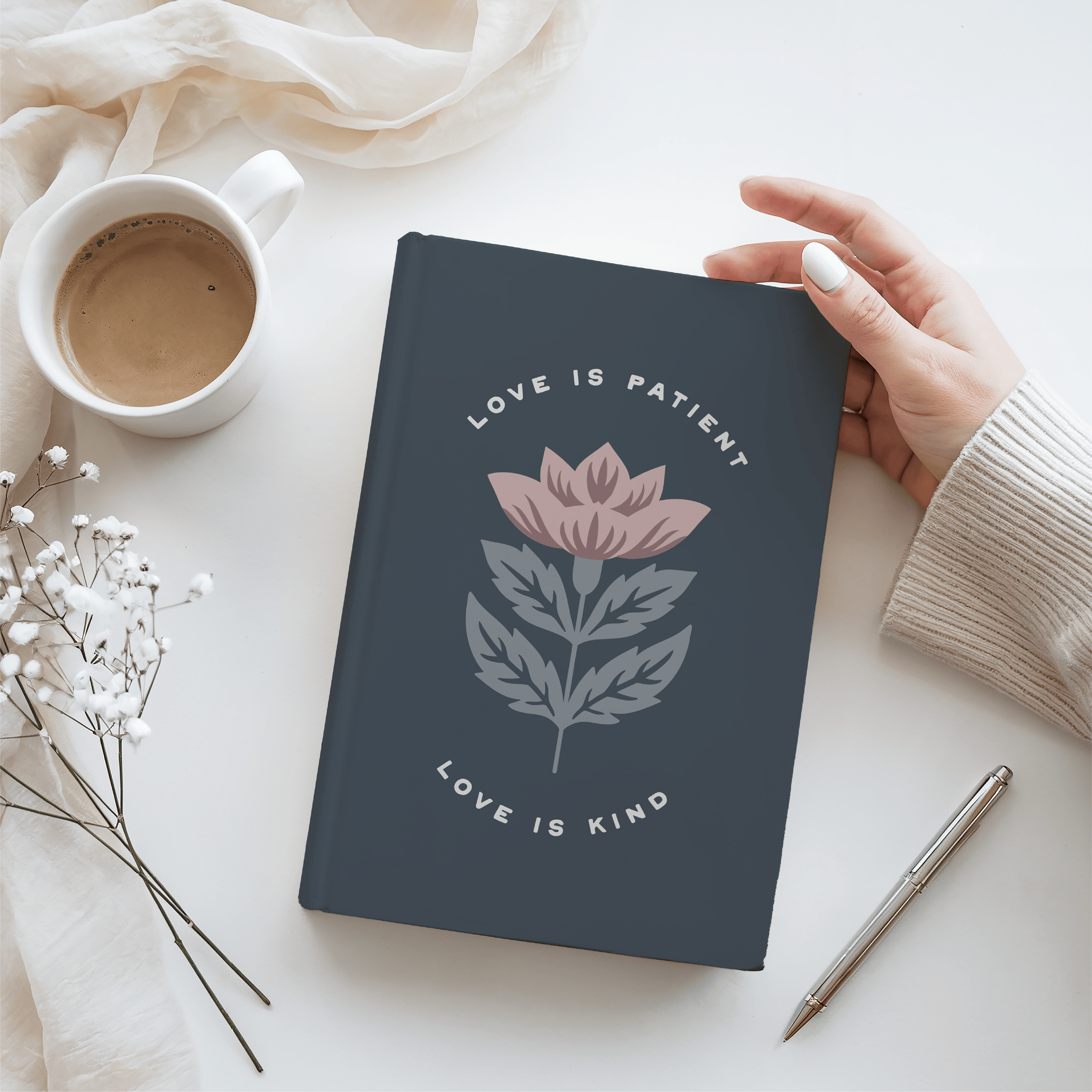 Notebook with floral design and text on a white surface with a cup of coffee and pen.