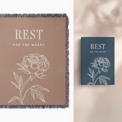 Brown blanket with floral design and text 'REST FOR THE WEARY' next to a blue book with the same design.