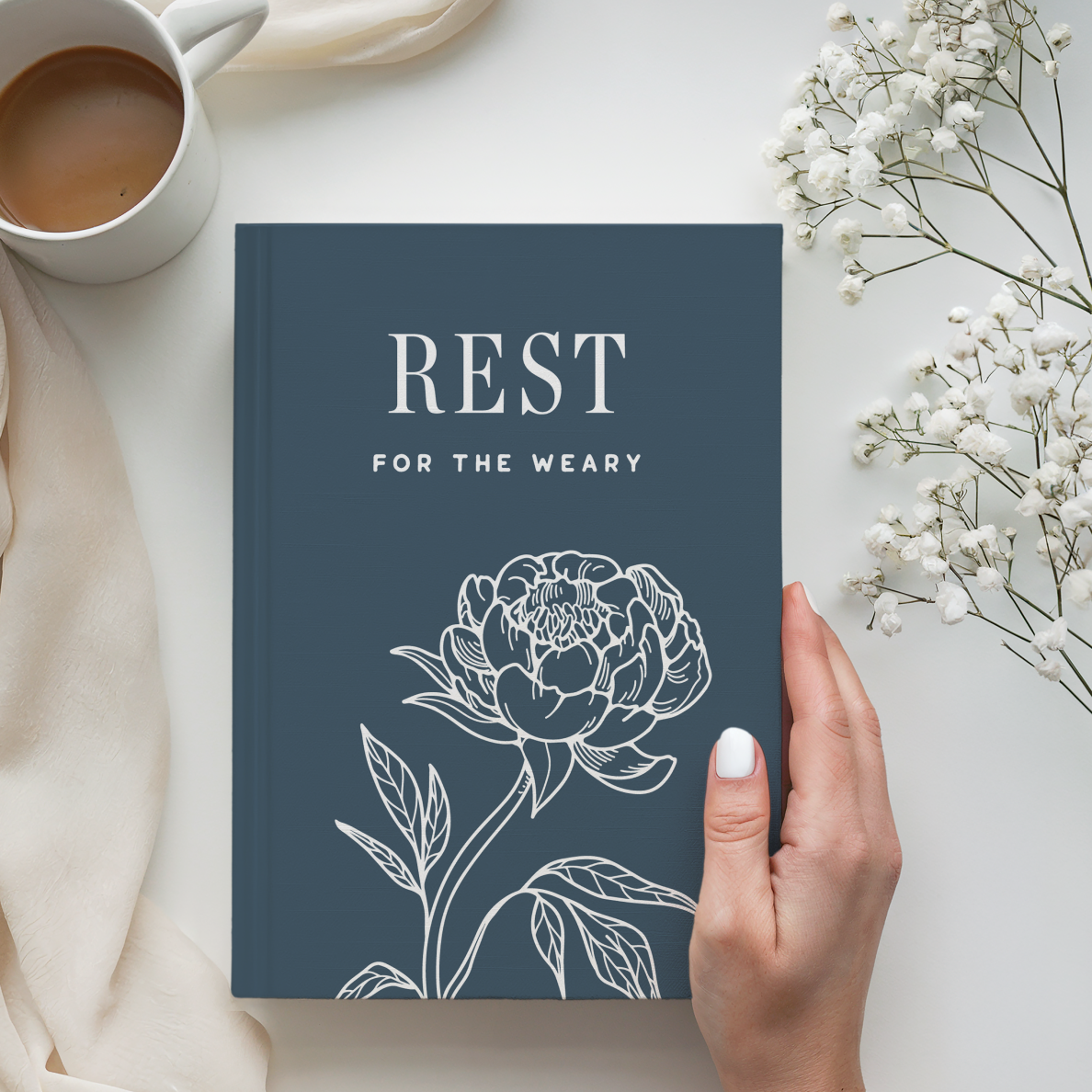 Book titled 'REST FOR THE WEARY' with a floral design on a light surface with a cup of coffee and flowers.