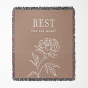 Blanket with floral design and text 'REST FOR THE WEARY' on a beige background