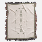 Blanket with 'Rooted' text and fringes on a white background