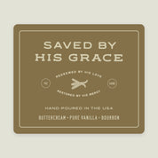 White jar candle labeled “Saved by His Grace” with a gold lid. Vanilla bean scent and Christian message—faith-filled gift celebrating God’s redeeming love.