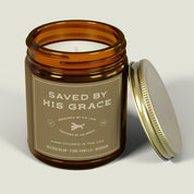 White jar candle labeled “Saved by His Grace” with a gold lid. Vanilla bean scent and Christian message—faith-filled gift celebrating God’s redeeming love.