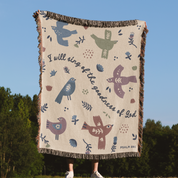 Person holding a decorative blanket with bird patterns and text against a natural background