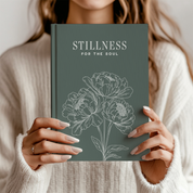 Person holding a book titled 'Stillness for the Soul' with floral design on cover