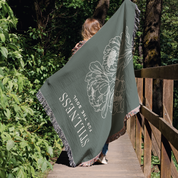 Person holding a green blanket with floral design and text in a forest setting