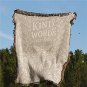 Neutral-toned woven blanket with the phrase “Kind words are like honey,” floral accents, and a honey bee; made of 100% cotton with fringe, perfect Christian gift.